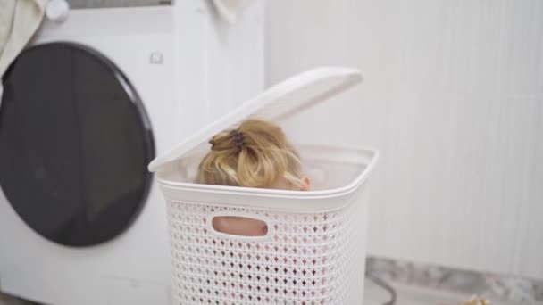 Grappig klein meisje blond spelen verstoppertje in badkamer in wasmand. — Stockvideo