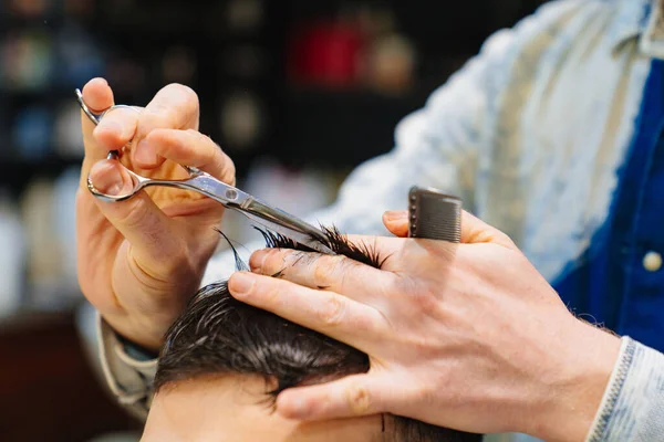 Fryzjer robi fryzurę dla bruneta z nożyczkami u fryzjera — Zdjęcie stockowe