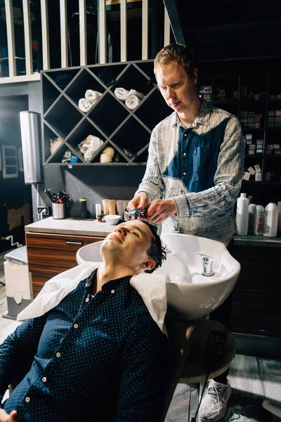Brunet człowiek myje włosy z fryzjerem w fryzjer. — Zdjęcie stockowe