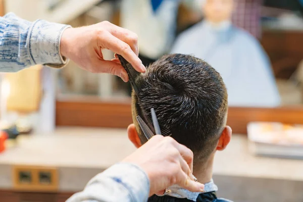Penata rambut membuat potong rambut untuk seorang pria brunet dengan gunting di salon Stok Foto