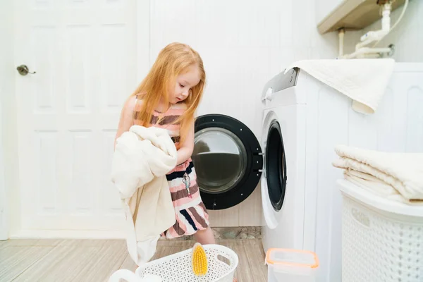 Uma menina bonito coloca lavanderia na máquina de lavar roupa. — Fotografia de Stock