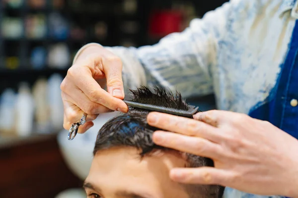 Frisør gør en frisure til en brunet mand med en saks i en barbershop Royaltyfrie stock-fotos