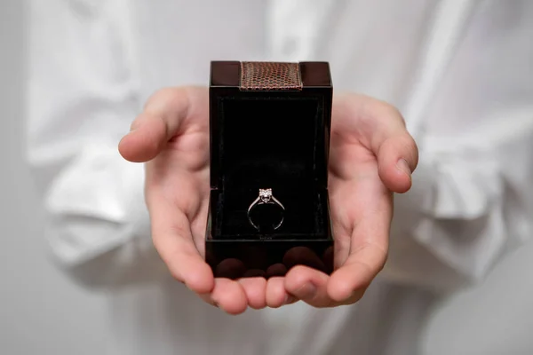 A young man holds in his hands a jewelry box with a diamond ring inside — Stock Photo, Image