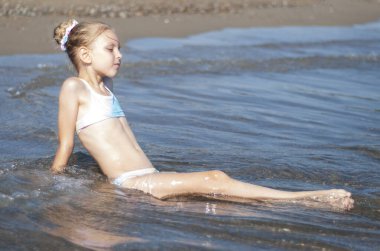 Deniz kıyısında mayo giymiş küçük bir kız oynuyor.