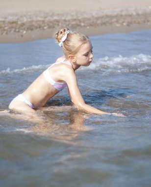 Deniz kıyısında mayo giymiş küçük bir kız oynuyor.