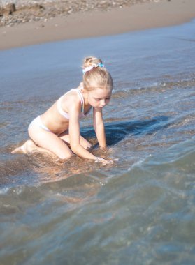 Deniz kıyısında mayo giymiş küçük bir kız oynuyor.