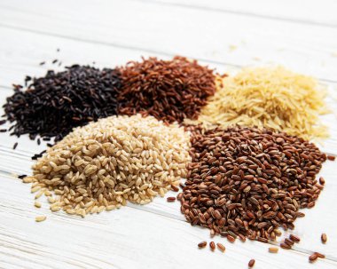 Beyaz ahşap zemin üzerinde çeşitli pirinç seti: siyah, basmati, kahverengi ve kırmızı karışık pirinç