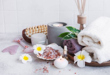 Spa seti, temel yağ, masaj tuzu, mum ve gri beton arka planda Frangipani çiçekleri