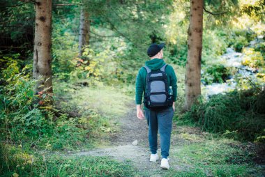 Sırt çantalı bir adam sonbahar ormanında yürüyor. Sonbahar orman patikalarında tek başına yürüyüş. Seyahat kavramı.