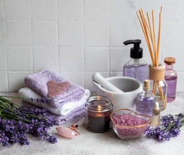 Lavanta kaplıcası. Gerekli yağlar, deniz tuzu, havlular ve yüz silindiri. Lavanta çiçekli doğal bitki kozmetiği.