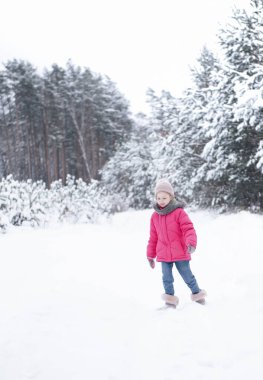 Parlak ceketli küçük bir kız kışın karlı ormanda oynar..