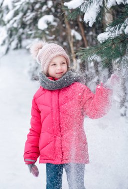Parlak ceketli küçük bir kız kışın karlı ormanda oynar..