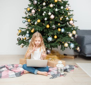 Büyük bir oturma odasında Noel ağacı. Küçük kız Noel ağacının yanında oynuyor. Bilgisayarı olan bir kız arkadaşlarıyla iletişim kurar..