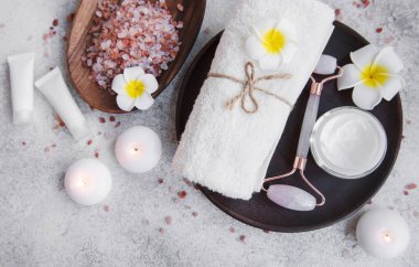Spa seti, temel yağ, masaj tuzu, mum ve gri beton arka planda Frangipani çiçekleri