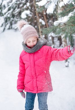 Parlak ceketli küçük bir kız kışın karlı ormanda oynar..