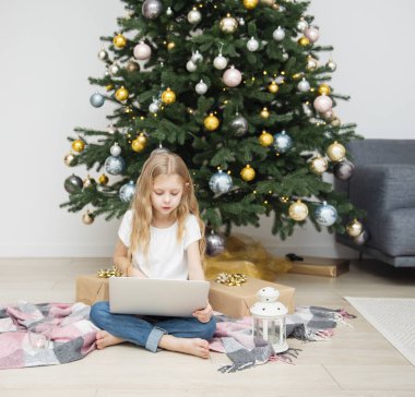 Büyük bir oturma odasında Noel ağacı. Küçük kız Noel ağacının yanında oynuyor. Bilgisayarı olan bir kız arkadaşlarıyla iletişim kurar..