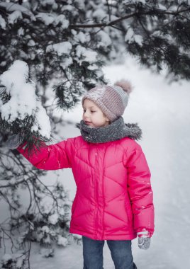 Parlak ceketli küçük bir kız kışın karlı ormanda oynar..
