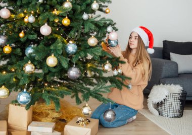 Genç kız Noel ağacını süslüyor. Oturma odasında Noel ağacı.