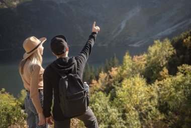 Dağlarda seyahat eden genç bir çift. Bir adam, doğa geçmişi olan bir dağa işaret ediyor.
