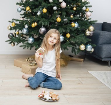 Oturma odasındaki Noel ağacının yanında zencefilli ekmek yiyen kız.