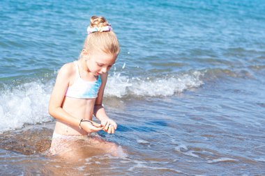 Deniz kıyısında mayo giymiş küçük bir kız oynuyor.