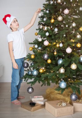 Hediyeli çocuk Noel ağacının yanında oynuyor. Oturma odasının içi Noel ağacı ve süslemelerle dolu. Yeni yıl. Hediye vermek.