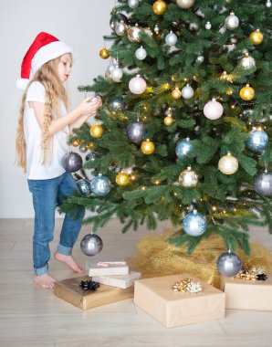 Hediyeli bir kız Noel ağacının yanında oynuyor. Oturma odasının içi Noel ağacı ve süslemelerle dolu. Yeni yıl. Hediye vermek.