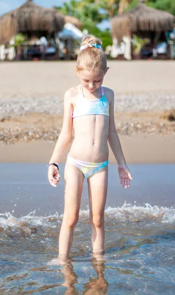 Deniz kıyısında mayo giymiş küçük bir kız oynuyor.