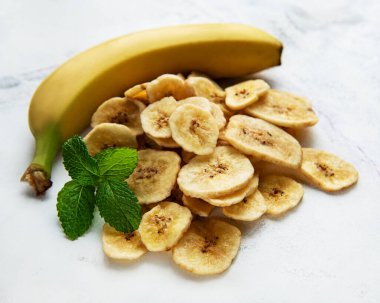 Beyaz mermer arka planda kurutulmuş muz dilimleri veya cips.