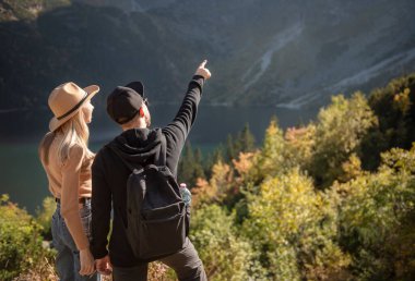 Dağlarda seyahat eden genç bir çift. Bir adam, doğa geçmişi olan bir dağa işaret ediyor.