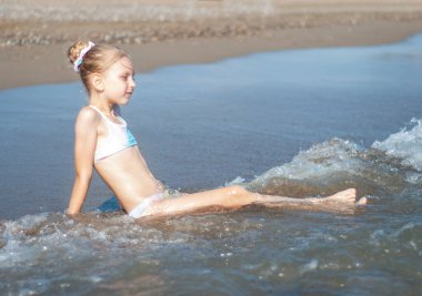 Deniz kıyısında mayo giymiş küçük bir kız oynuyor.