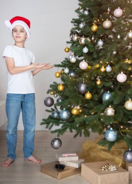 Hediyeli çocuk Noel ağacının yanında oynuyor. Oturma odasının içi Noel ağacı ve süslemelerle dolu. Yeni yıl. Hediye vermek.