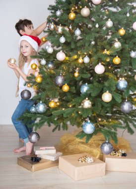 Çocuklar - bir oğlan ve bir kız Noel ağacının yanında oynuyorlar. Oturma odasının içi Noel ağacı ve süslemelerle dolu. Yeni yıl. Hediye vermek.
