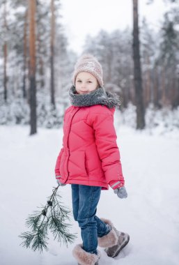 Parlak ceketli küçük bir kız kışın karlı ormanda oynar..
