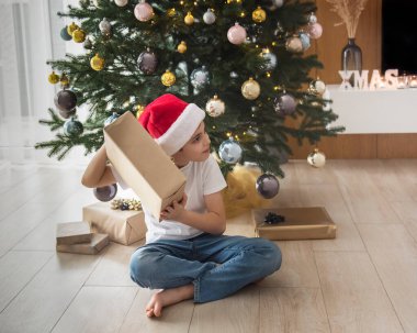 Hediyeli çocuk Noel ağacının yanında oynuyor. Oturma odasının içi Noel ağacı ve süslemelerle dolu. Yeni yıl. Hediye vermek.