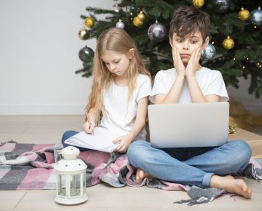 Büyük bir oturma odasında Noel ağacı. Çocuklar Noel ağacının yanında oynuyorlar. Dizüstü bilgisayarı olan bir çocuk arkadaşlarıyla iletişim kurar..