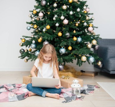 Büyük bir oturma odasında Noel ağacı. Küçük kız Noel ağacının yanında oynuyor. Bilgisayarı olan bir kız arkadaşlarıyla iletişim kurar..