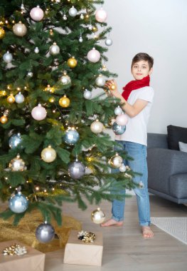 Hediyeli çocuk Noel ağacının yanında oynuyor. Oturma odasının içi Noel ağacı ve süslemelerle dolu. Yeni yıl. Hediye vermek.