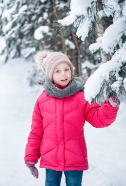 Parlak ceketli küçük bir kız kışın karlı ormanda oynar..