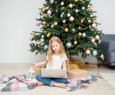 Büyük bir oturma odasında Noel ağacı. Küçük kız Noel ağacının yanında oynuyor. Bilgisayarı olan bir kız arkadaşlarıyla iletişim kurar..