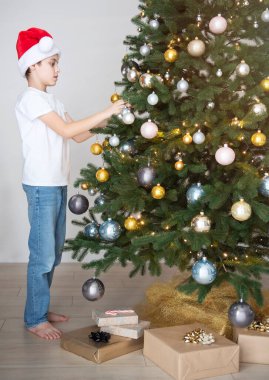 Hediyeli çocuk Noel ağacının yanında oynuyor. Oturma odasının içi Noel ağacı ve süslemelerle dolu. Yeni yıl. Hediye vermek.