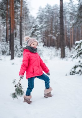 Parlak ceketli küçük bir kız kışın karlı ormanda oynar..