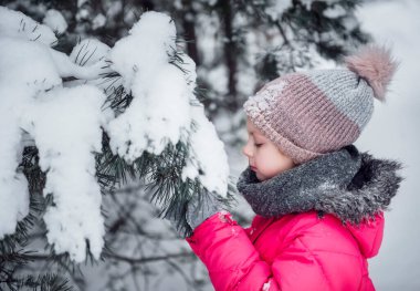 Parlak ceketli küçük bir kız kışın karlı ormanda oynar..