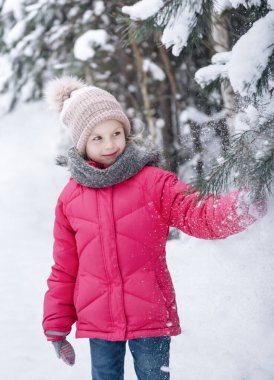 Parlak ceketli küçük bir kız kışın karlı ormanda oynar..