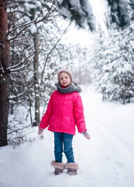 Parlak ceketli küçük bir kız kışın karlı ormanda oynar..