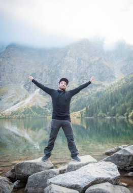 Elleri dağın tepesinde olan şapkalı genç turist doğaya hayran.