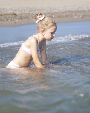 Deniz kıyısında mayo giymiş küçük bir kız oynuyor.