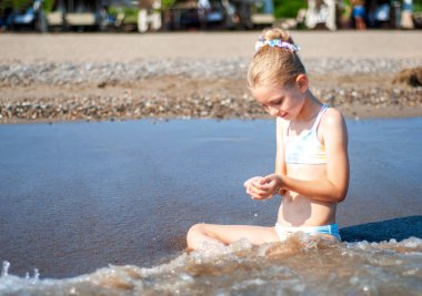 Deniz kıyısında mayo giymiş küçük bir kız oynuyor.