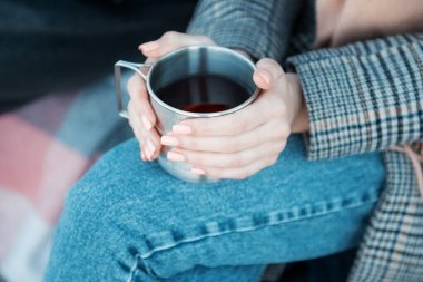 Elinde demir bardak ve sıcak çay tutan genç bir kadın. Kadın ellerinin sıcak bir bardak içeceği tuttuğu yakın plan. 