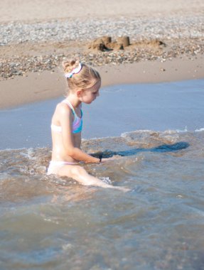 Deniz kıyısında mayo giymiş küçük bir kız oynuyor.